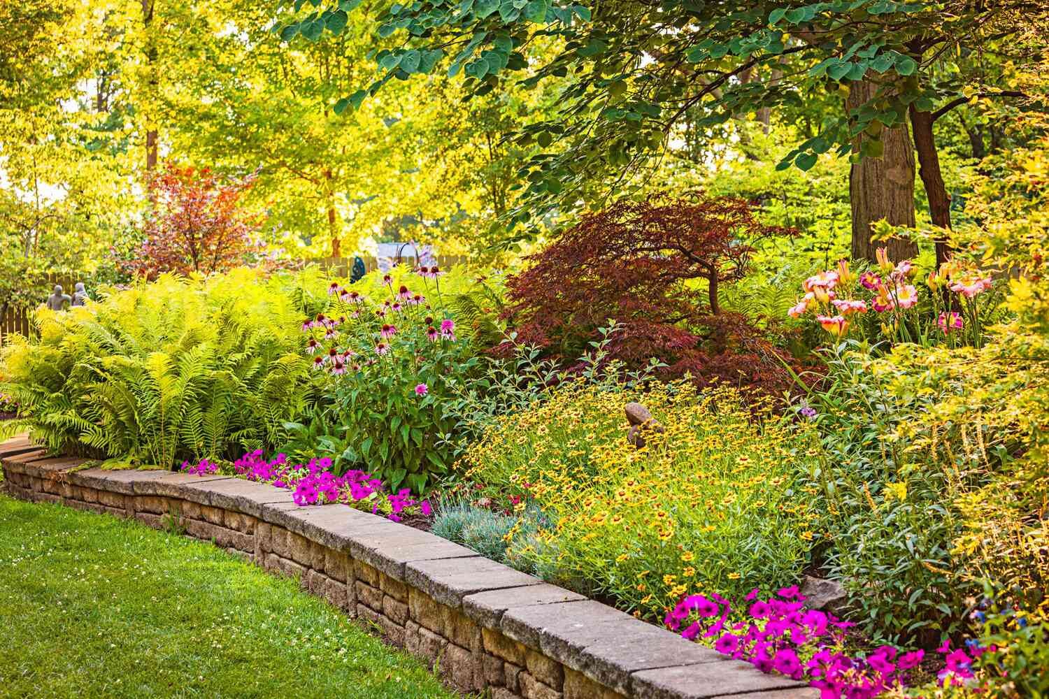 A lush planted border with pink and yellow flowers behind a stone retaining wall